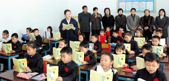 북한에서는 개교식이 끝나면 신입생들이 교실에 들어와 교장 선생님, 간부 선생님, 학부모가 지켜보는 가운데 새 학년 첫 수업을 들어요. 신입생들이 똑같은 교복을 입고, 똑같은 자세로 책을 읽고 있네요.