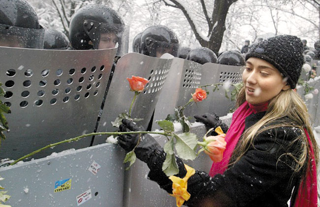 2004년 우크라이나에서는 여당 측의 부정선거를 규탄하는‘오렌지 혁명’이 일어났어요. 사람들은 야당을 상징하는 오렌지색의 옷·두건·목도리 등을 착용하고 오렌지색 깃발을 들고 나왔어요. 사진은 왼쪽 손목에 오렌지색 리본을 맨 시민이 경찰 방패에 꽃을 꽂고 있는 모습. /위키피디아